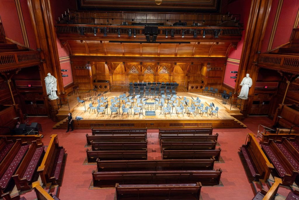 Wide shot of Sanders Theatre with dozens of chairs on stage, taken before a concert 